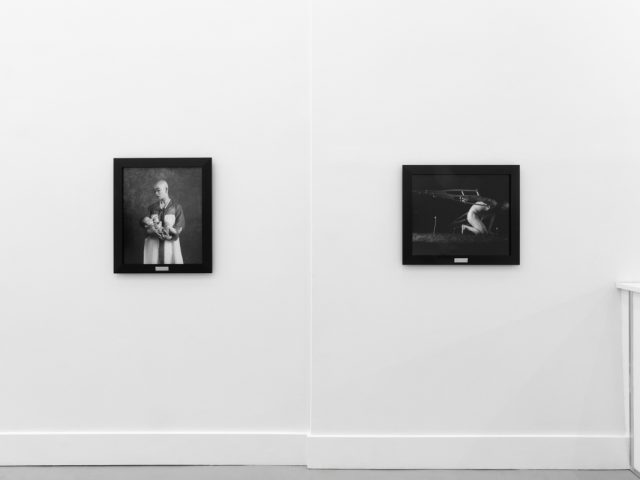 A photograph of black and white photographs in black frames hanging in a contemporary gallery setting.