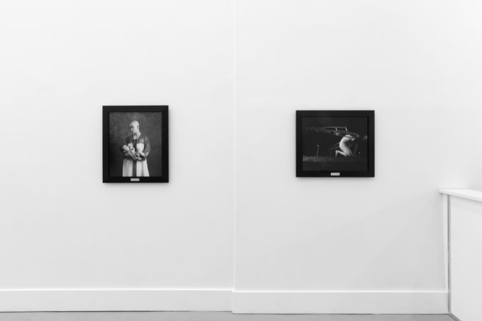 A photograph of black and white photographs in black frames hanging in a contemporary gallery setting.