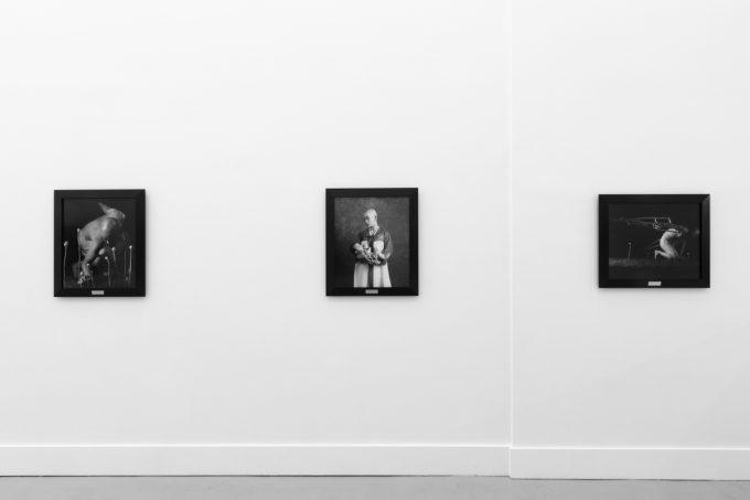 A photograph of black and white photographs in black frames hanging in a contemporary gallery setting.