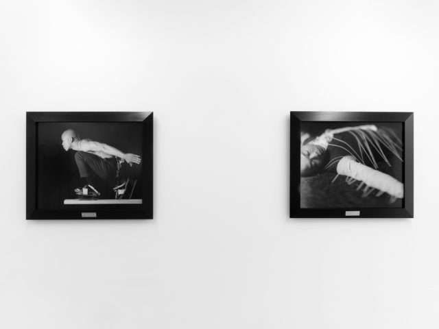 A photograph of black and white photographs in black frames hanging in a contemporary gallery setting.