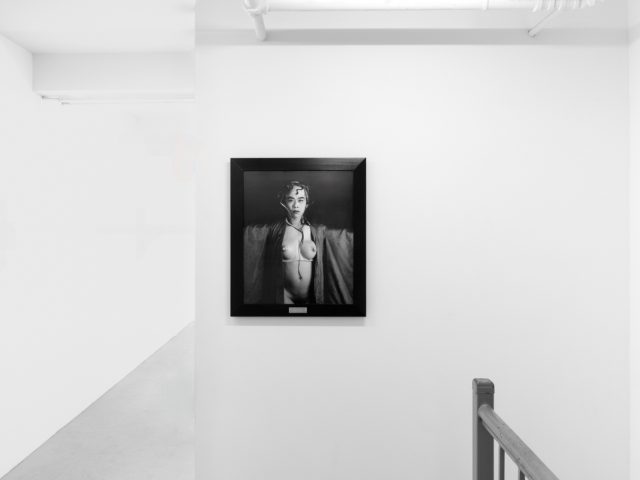 A photograph of black and white photographs in black frames hanging in a contemporary gallery setting.