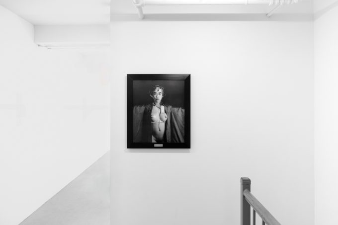 A photograph of black and white photographs in black frames hanging in a contemporary gallery setting.