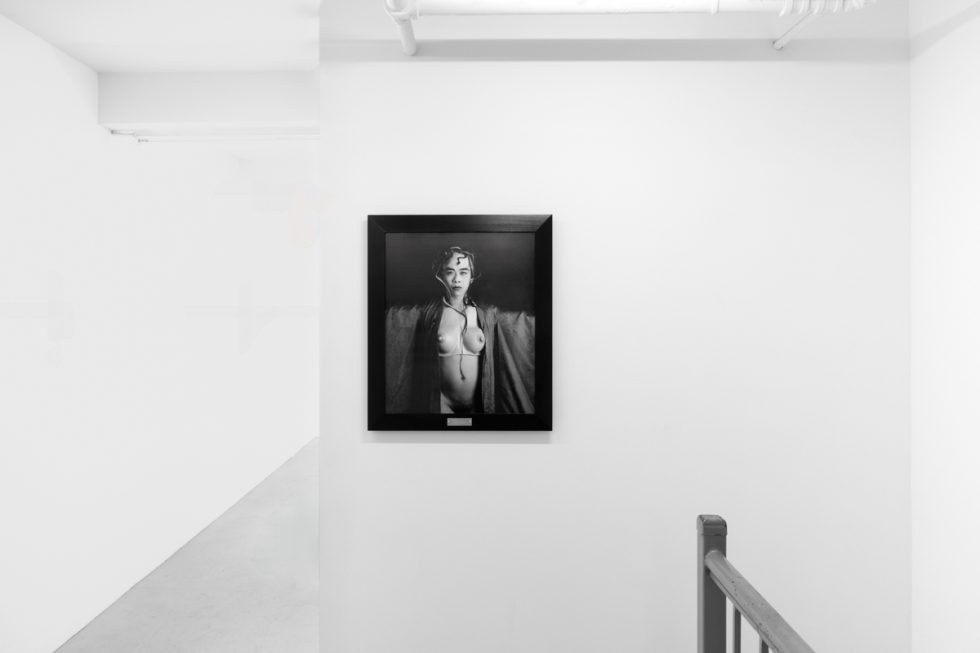 A photograph of black and white photographs in black frames hanging in a contemporary gallery setting.