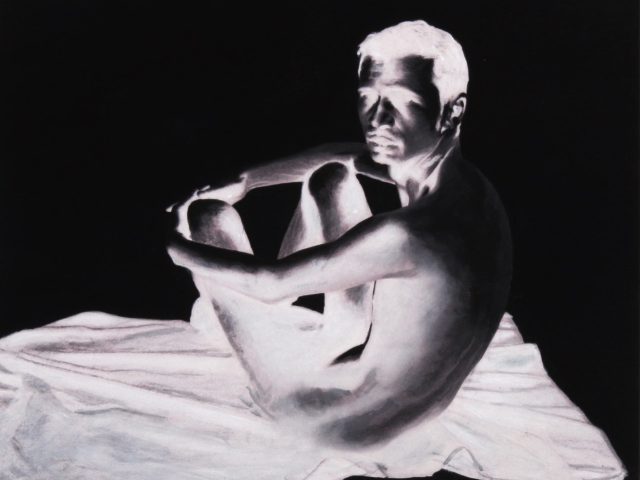 A black and white photograph of a man sitting clutching his knees.