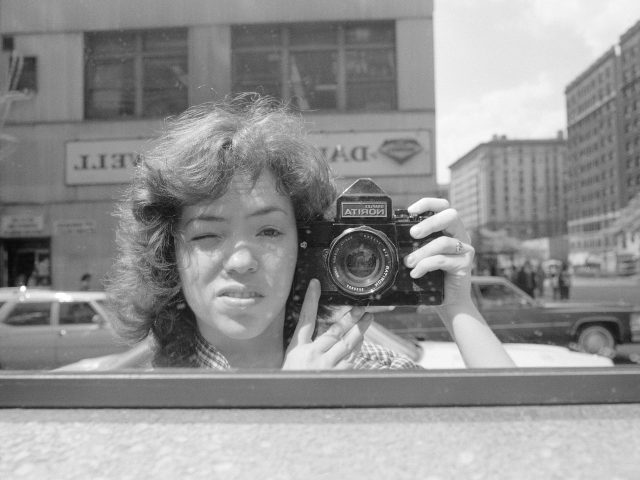 A black and white photo of a woman in a mirror on the street