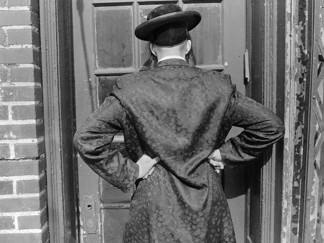 A black and white photograph of a man's back with his hands on his hips.