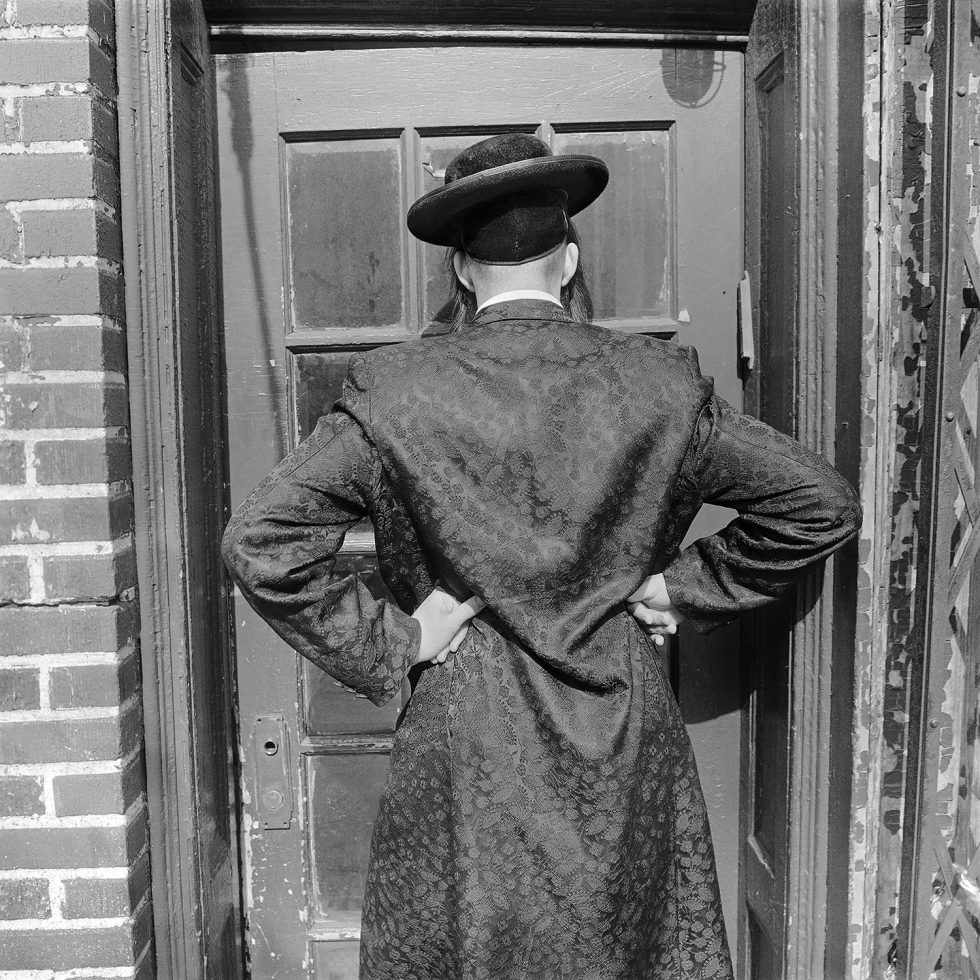 A black and white photograph of a man's back with his hands on his hips.