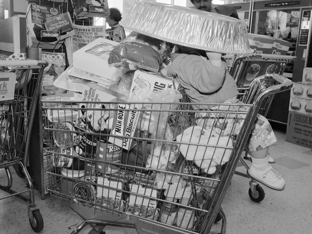 A black and white photograph of a child in a shopping cart in a supermarket.