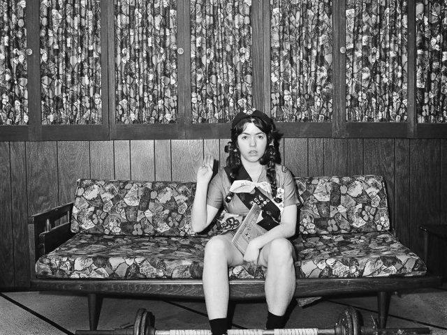 A black and white photograph of a girl sitting on a sofa doing the girl scout oath.