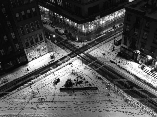 A black and white photograph of cross streets with snow.