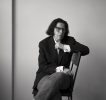 A black and white photograph of a skeptical looking person sitting in a chair.
