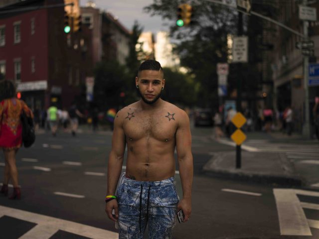 A handsome young man stands in a New York City street with star tattoos on his skin.