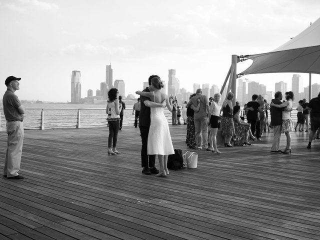 A black and white photograph of people tango dancing on a pier.