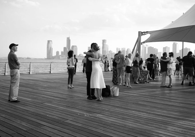 A black and white photograph of people tango dancing on a pier.