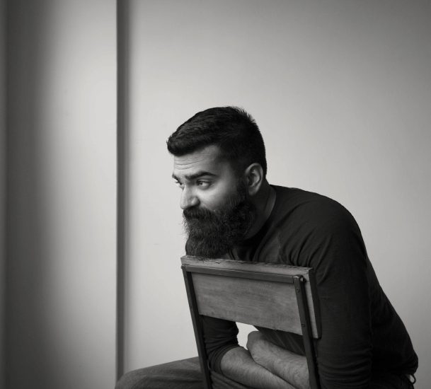 A black and white photograph of a man sitting backwards in a chair lost in thought.