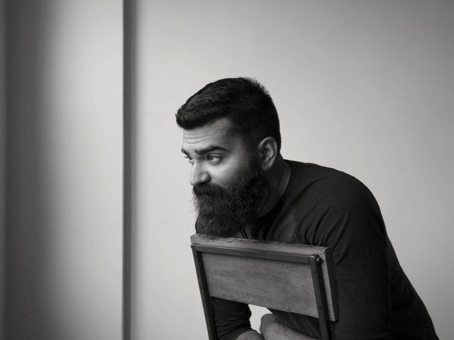 A black and white photograph of a man sitting backwards in a chair lost in thought.