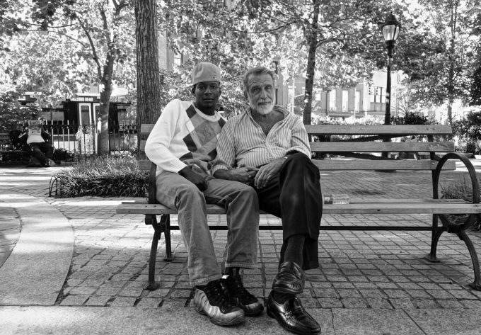 A black and white photograph of two men sitting on a bench in a park.
