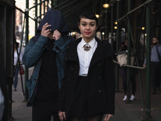 A color photograph of a young woman in the middle of a busy sidewalk.
