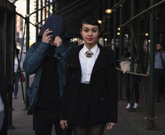 A color photograph of a young woman in the middle of a busy sidewalk.