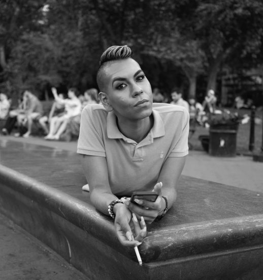 A black and white portrait of a person relaxing on the edge of a fountain in washington square park.
