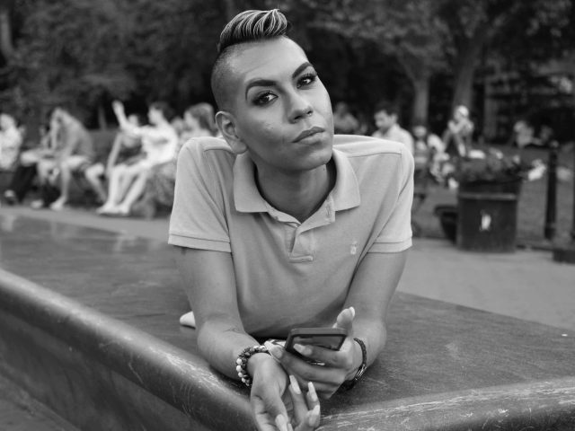 A black and white portrait of a person relaxing on the edge of a fountain in washington square park.