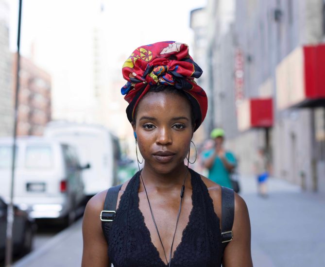 A photograph of a young woman on the street staring at the camera.