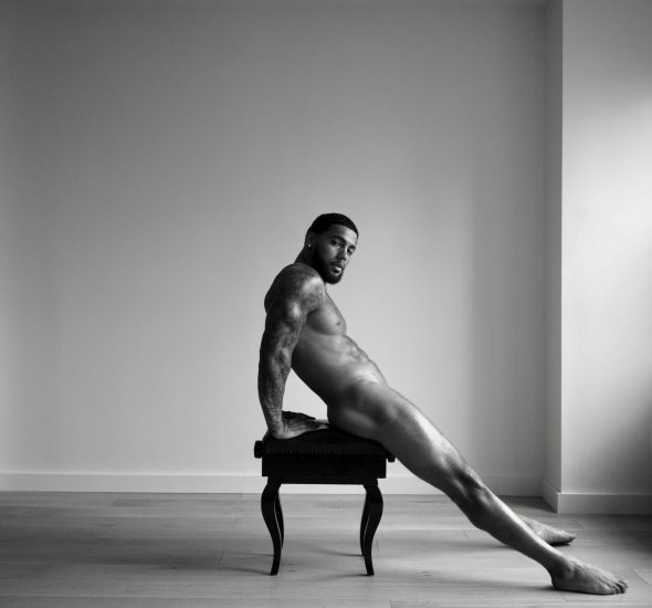 A black and white portrait of a nude man sitting on a piano bench.