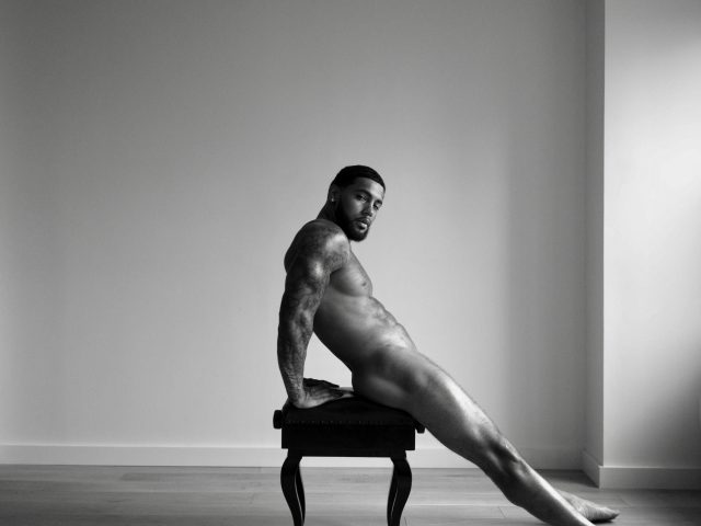 A black and white portrait of a nude man sitting on a piano bench.