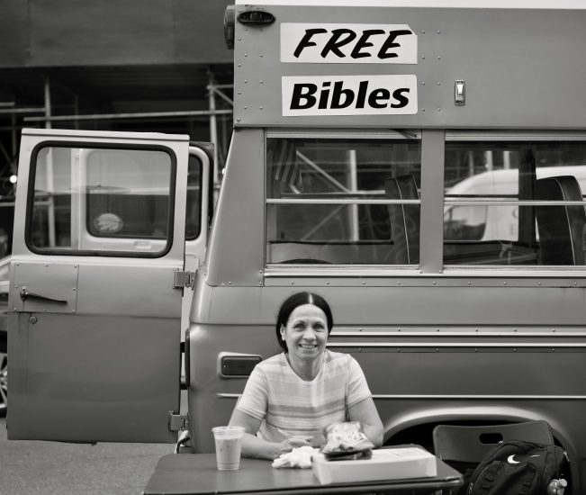 A black and white photograph of a woman handing out free bibles.