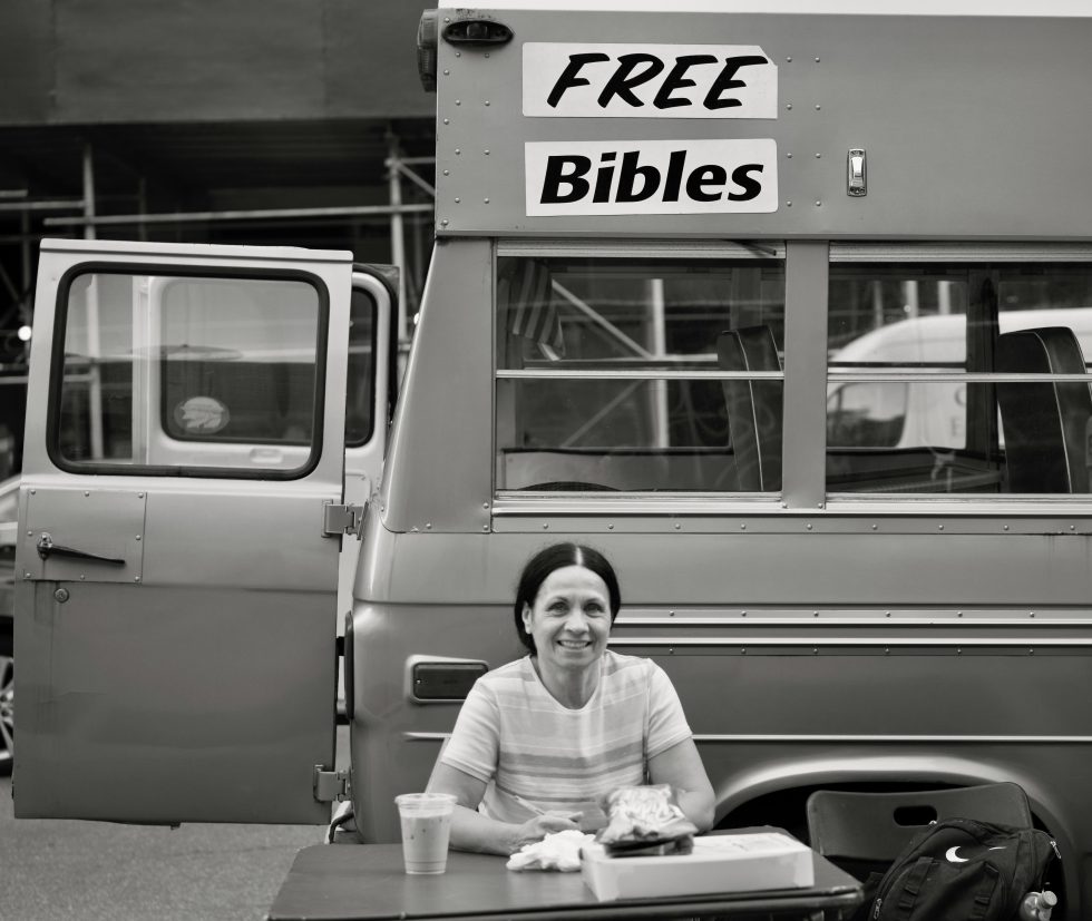 A black and white photograph of a woman handing out free bibles.