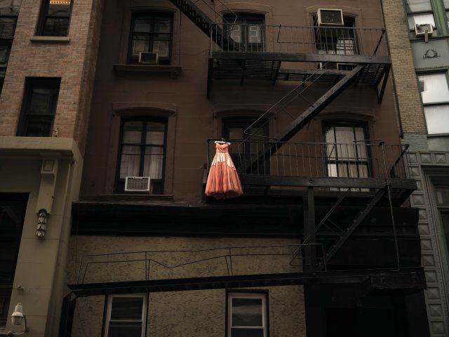 A color photograph of a pink dress hanging on a fire escape.