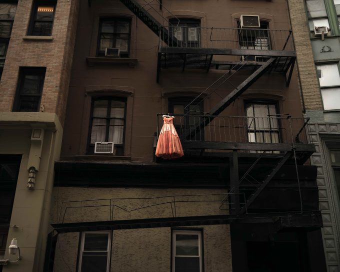 A color photograph of a pink dress hanging on a fire escape.