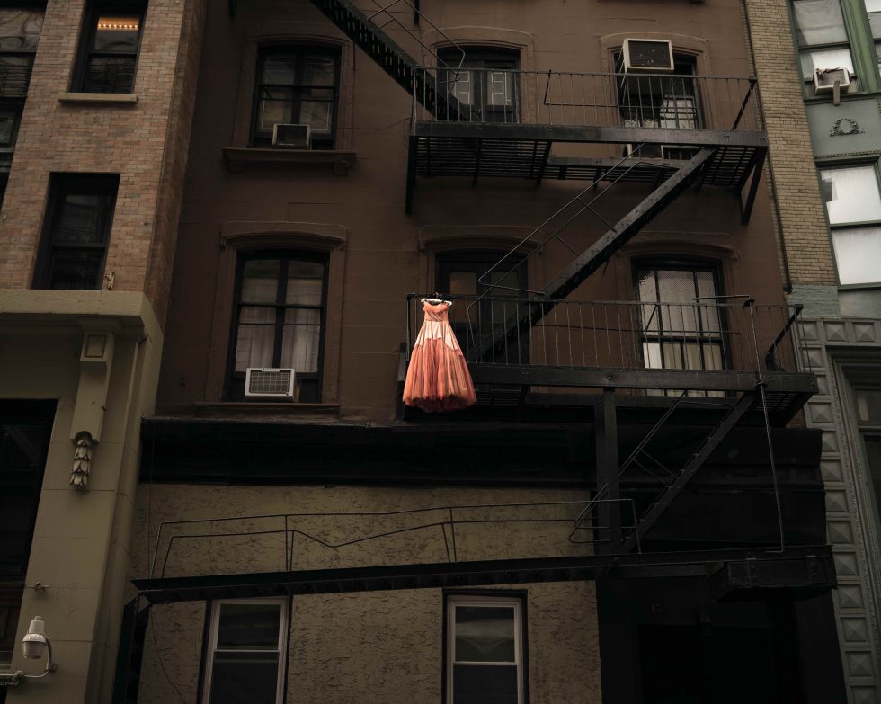 A color photograph of a pink dress hanging on a fire escape.