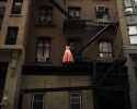 A color photograph of a pink dress hanging on a fire escape.