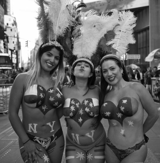 A black and white photograph of three women in carnival outfits in Times Square.