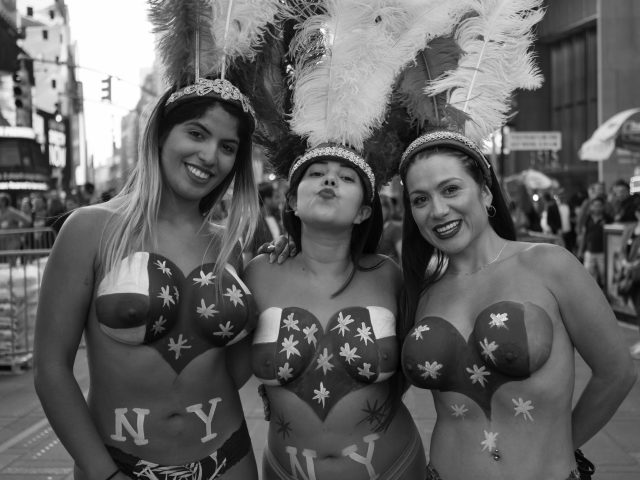 A black and white photograph of three women in carnival outfits in Times Square.