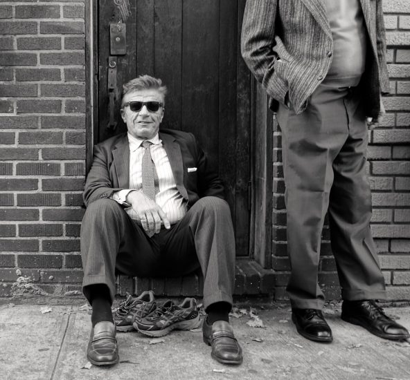 A black and white photograph of a man sitting on a stoop.