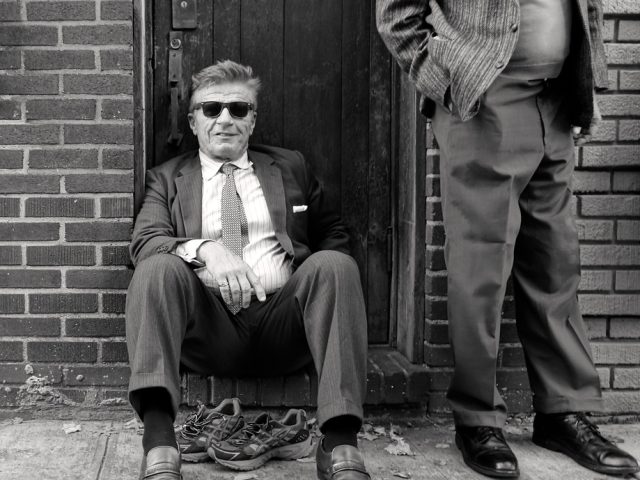 A black and white photograph of a man sitting on a stoop.