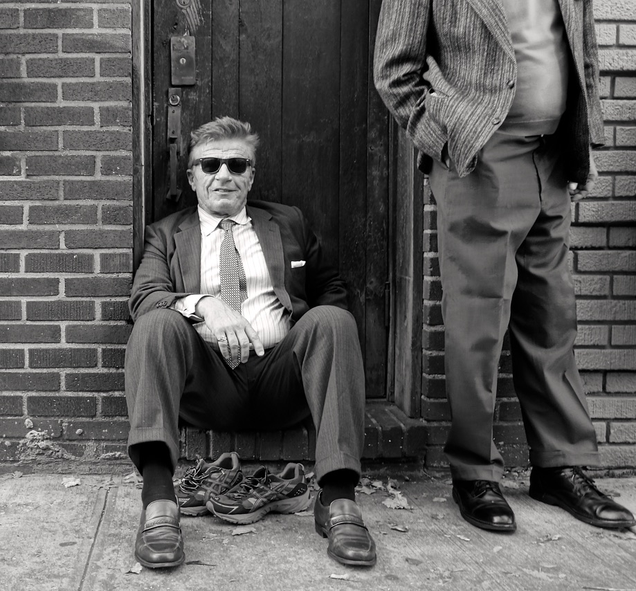 A black and white photograph of a man sitting on a stoop.