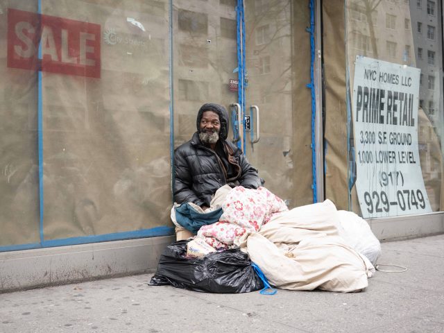 A photograph of a homeless man with a blanket on a city street.
