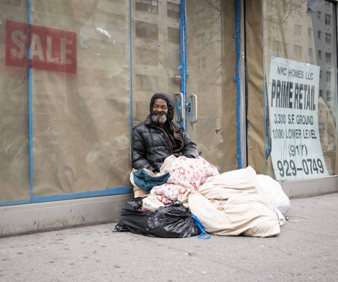 A photograph of a homeless man with a blanket on a city street.