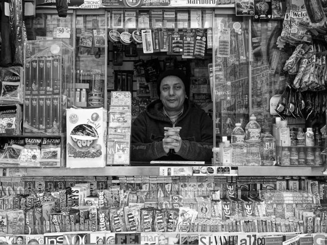 A black and white photograph of a man inside his newsstand.