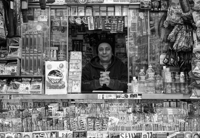 A black and white photograph of a man inside his newsstand.
