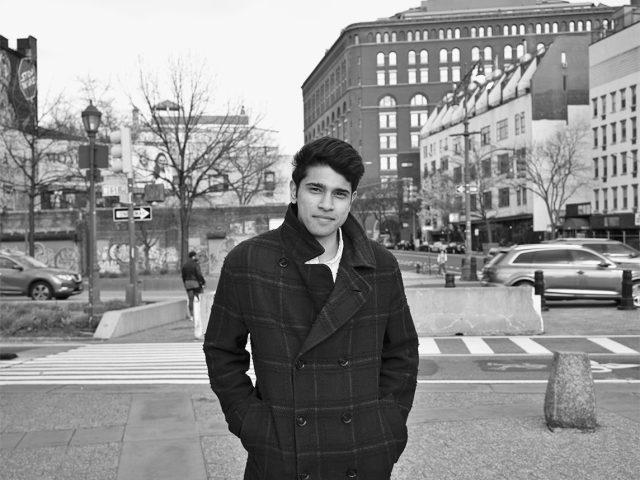 A black and white photograph of a man standing outside in a public space.