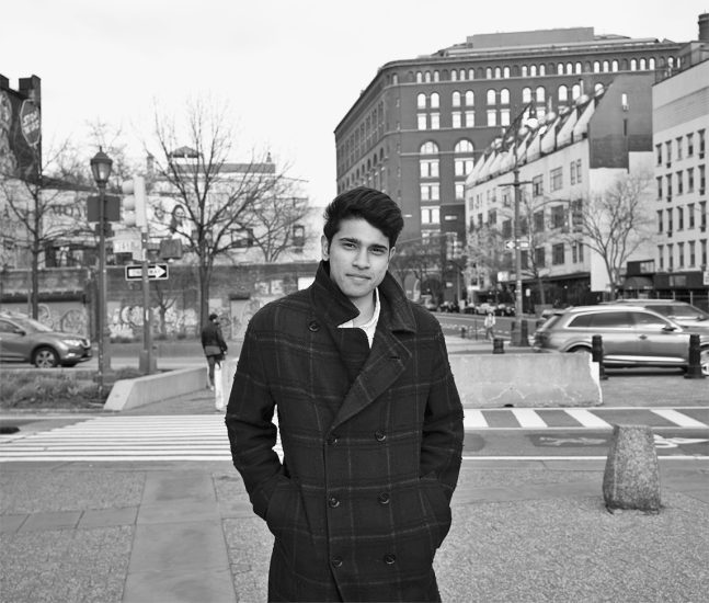 A black and white photograph of a man standing outside in a public space.