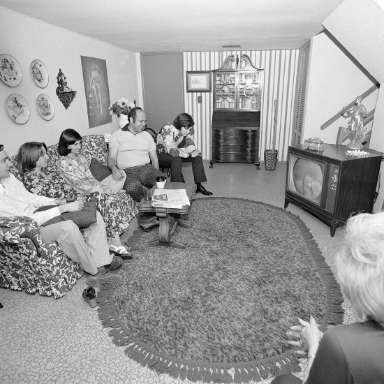 A black and white photograph of a family sitting in a suburban living room.