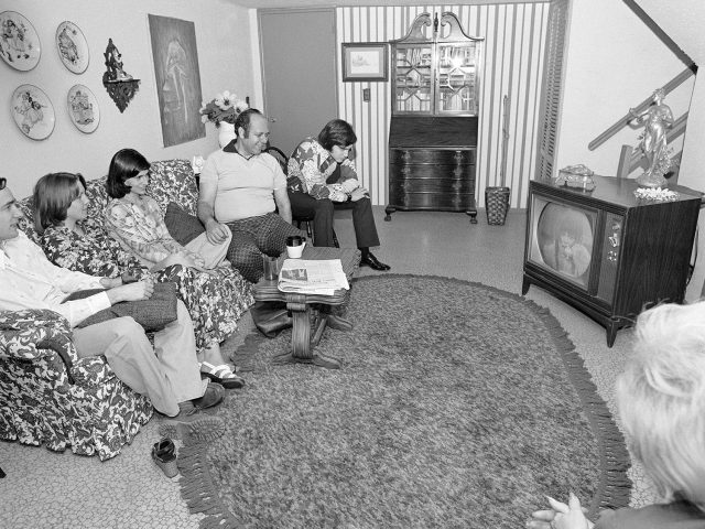 A black and white photograph of a family sitting in a suburban living room.