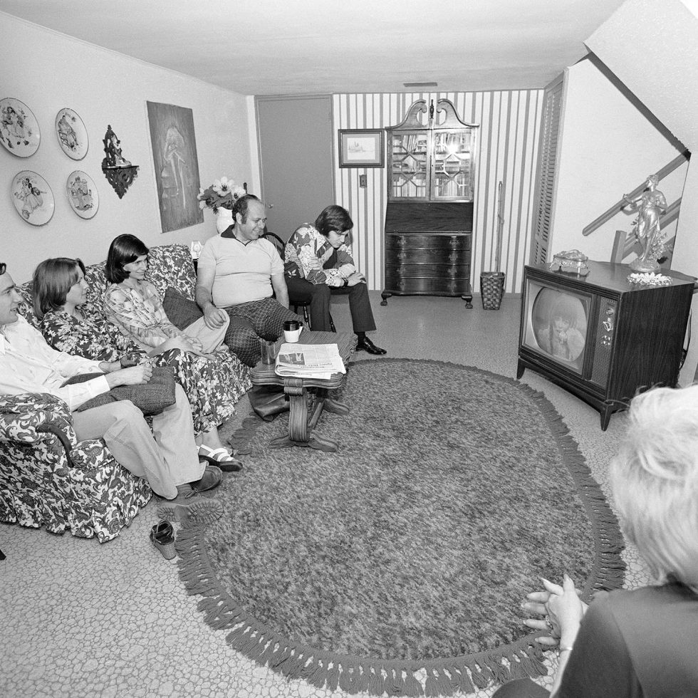 A black and white photograph of a family sitting in a suburban living room.