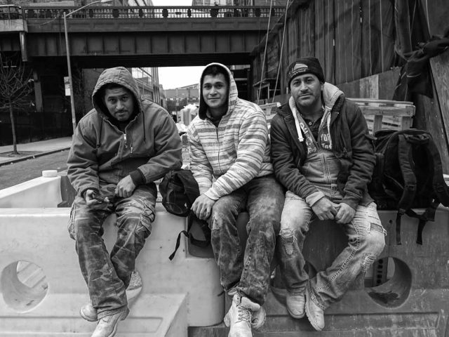 A black and white photograph of three men sitting on a barricade at the end of the work day.