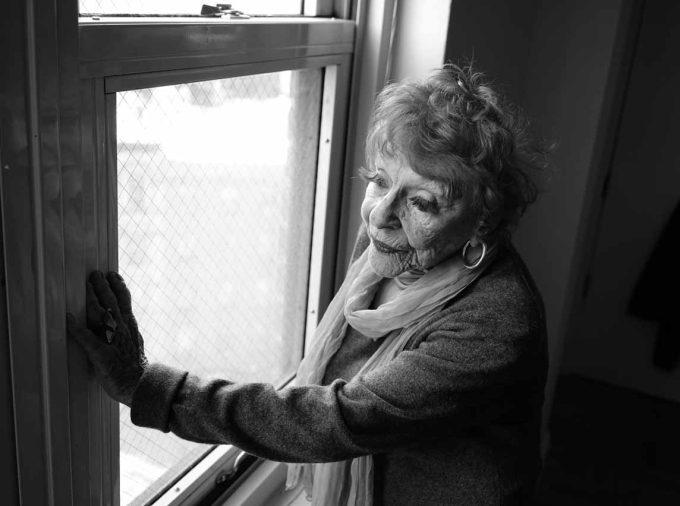 A black and white photograph of an older woman standing in a window.